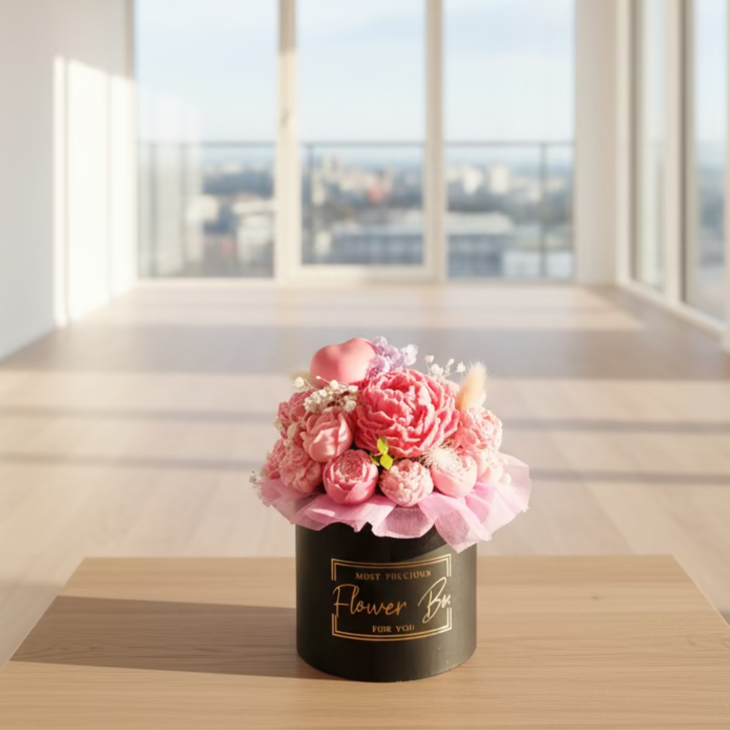 Pink floral arrangement in a black box on a wooden table with a cityscape view.